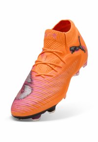 Scarpa da calcio arancione brillante con accenti rosa sfumati, superiore testurizzato, chiusura con lacci e logo nero. Adatta per superfici in erba compatta.