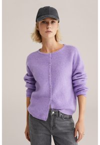 Ljuslila cardigan med mjuk textur, med rund halsringning, knappstängning och upprullade ärmar. Matchas med grå jeans.