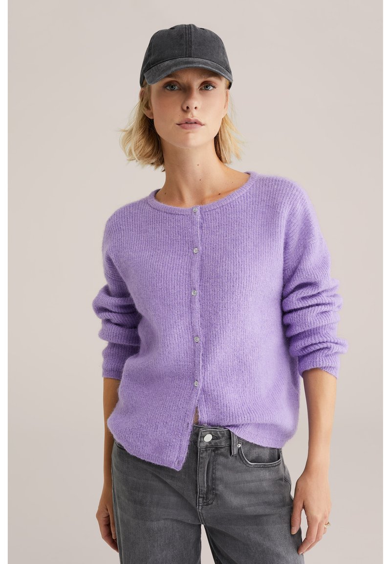 Ljuslila cardigan med mjuk textur, med rund halsringning, knappstängning och upprullade ärmar. Matchas med grå jeans.