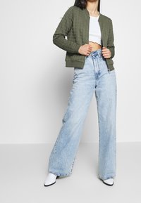 Olivgrön, kviltad bomberjacka med rund krage, parat med ljusblå, högmidjade byxor med vida ben och vita, spetsiga ankle boots.