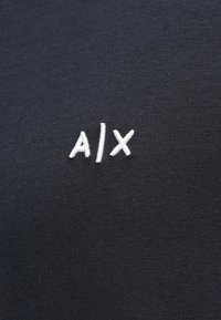 Čierne bavlnené tričko s bielym vyšitým logom "A|X" v jednoduchom sans-serif písmene, so hladkým, textúrovaným povrchom látky.