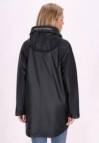 Melns ūdensizturīgs lietusmētelis ar kapuci, ar drukātu etiķeti uz apkakles, brīvs piegriezums un gluda, spīdīga faktūra.