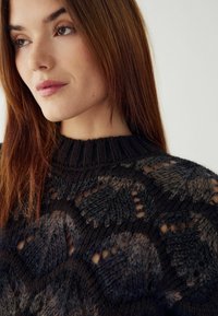 Prašmatni megztinis tamsiomis spalvomis su tekstūruota raštą, kuriame yra atvirų audinių elementų ir įgilinta apykaklė. Minkšta medžiaga su įvairiomis spalvomis.