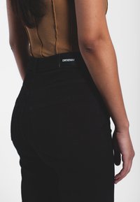 Jeans negros de cintura alta con bolsillos traseros, con una textura sólida y etiqueta DRDENIM en la cinturilla. La parte superior es de tela acanalada color beige.