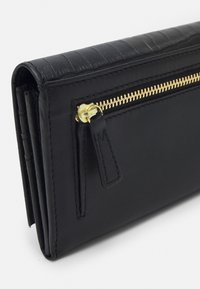 Svart läderplånbok med en texturerad ovansida, gyllene dragkedja och en slimmad design. Har flera kortfack och ett dragkedjefack.