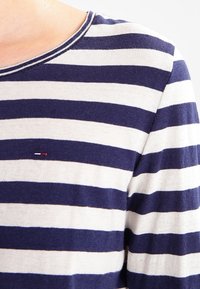 Marineblauwe en crèmekleurige gestreepte blouse met lange mouwen, een ronde hals en een klein logo-detail op de borst. Zachte stoftextuur.