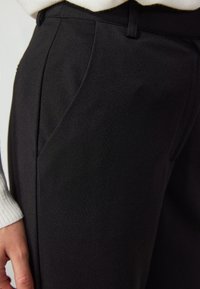 Pantalones negro hechos de una tela suave con un ajuste entallado, que cuentan con bolsillos laterales y un ligero brillo. Los detalles incluyen costuras rectas y una cinturilla.