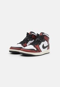 Bílé, černé a červené vysoké tenisky s texturovaným svrškem, černými tkaničkami a gumovou podrážkou, která se vyznačuje klasickým designem Air Jordan.