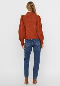 Pull texturé couleur rouille avec manches ballon, associé à un jean bleu taille haute. La tenue est complétée par des chaussures marron à talons.