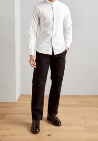 Witte langemouwen shirt met een Mandarin kraag, zwarte broek en bruine leren schoenen. Gepolijst stof en op maat gemaakt fit. Eenvoudige knoopsluiting.