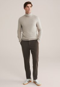 Gai pelēks turtlenecka džemperis apvienots ar tumšām šaurām biksēm un zaļgani pelēkiem sporta apaviem ar baltām svītrām. Gluda tekstūra, moderna piegriezuma.