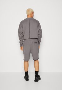 Grijze sweatshirt met een relaxed fit, bijpassende grijze shorts met een onafgewerkte zoom en zwarte schoenen. Minimalistisch ontwerp en zachte stoftextuur.
