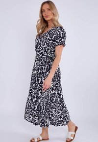 Black and white printed dress with short sleeves, a cinched waist, and a flowing skirt. Worn with white sandals, feature a rounded strap design.