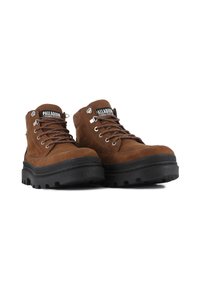 Bottes de randonnée en suède marron avec des semelles en caoutchouc noires, dotées d'œillets en métal et de lacets, ainsi que d'une languette de marque.