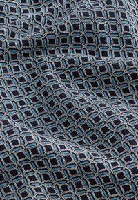 Tengerészkék szövet, amely világoskék és szürke színű, összekapcsolt hatszögekből álló geometriai mintát ábrázol, látható textúrával és mélységgel.