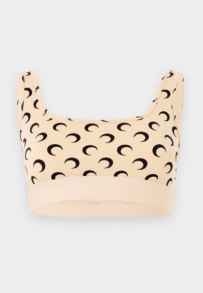 Μπεζ αθλητικό σουτιέν με φαρδιές τιράντες που έχουν επαναλαμβανόμενο μαύρο μοτίβο ημισελήνου και ελαστική ταινία στο κάτω μέρος.