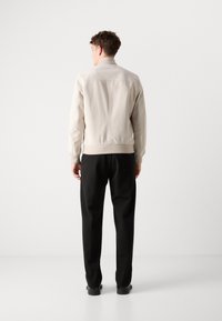 Beez bomber-jakk, millel on soonilised varrukate otsad ja kaelus; minimalistlik disain, sile tekstuur, kantud mustade pükstega. Tagantvaates on näha puhtaid jooni ja õmblusi.