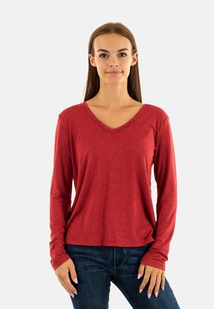 Rode langärmelige V-hals T-shirt met drie knopen op de halslijn, gemaakt van zachte stof, gecombineerd met donkerblauwe jeans.