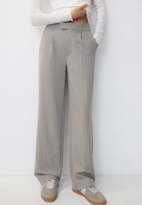 Pantalons larges gris clair en tissu lisse avec des plis à l'avant, associés à des baskets basses grises avec des accents blancs.