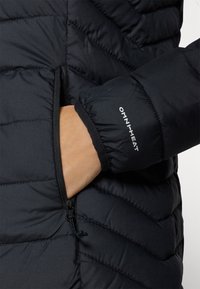 Giacca a vento nera con motivo trapuntato. Presenta una tasca con zip e un polsino elastico. Logo OMNI-HEAT stampato in bianco sulla manica.