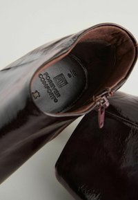 Burgunderfärgade lackstövlar i ankellängd med en slät finish, featuring en sidogzipper och en vadderad innersula märkt "Forever Comfort."