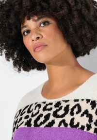 Strickpullover mit einem cremefarbenen Oberteil, schwarzem Leopardenmuster und einem lila Unterteil. Weiche Textur mit rundem, weitem Ausschnitt.