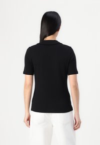 Polo shirt noir à manches courtes avec col, texture lisse, silhouette ajustée et design minimaliste. Pas de logos ni de motifs visibles.