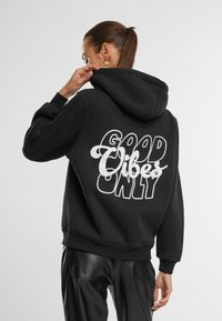 Black hoodie with a large white text design on the back that reads "GOOD VIBES ONLY." Features a drawstring hood and ribbed cuffs.