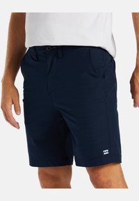Navy blue shorts made of lightweight fabric, featuring side pockets and a small logo on the lower left leg. Smooth texture, regular fit.