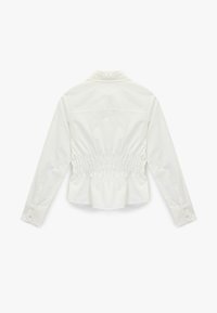 Camisa blanca con un diseño estructurado, mangas largas y detalle fruncido en la espalda. Cuenta con cuello y puños abotonados, confeccionada en tejido liso.