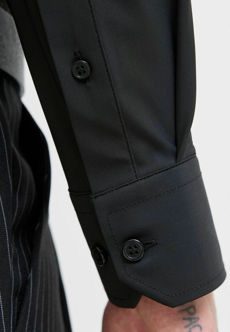 Schwarzes Hemdmanschette mit glatter Textur, ausgestattet mit zwei schwarzen Knöpfen und kontrastierenden Nähten. Der Stoff zeigt minimalen Glanz.