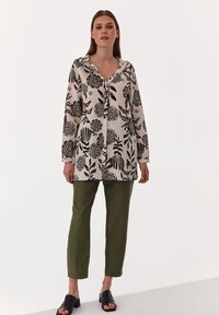 Camicia a maniche lunghe, con bottoni, color crema con stampa floreale nera; abbinata a pantaloni dritti verdi e sandali neri con fascia.