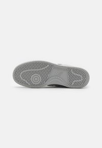 Grå sneakersål med mønstret slidbane. Har brandlogo og cirkulært detaljer. Lavet af gummimateriale for holdbarhed og greb.