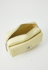 Yellow leather bag with silver zipper and hardware, rectangular shape, featuring a front logo accent and opened top view revealing interior lining.