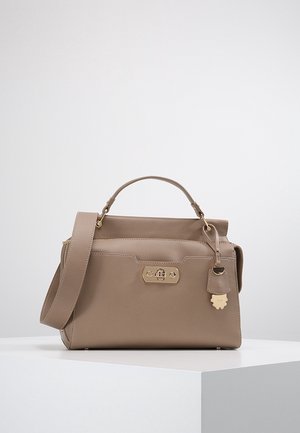 Beige leren handtas met bovenhandvat, verstelbare schouderriem, voorste gesp sluiting en decoratief hanglabel op witte ondergrond.