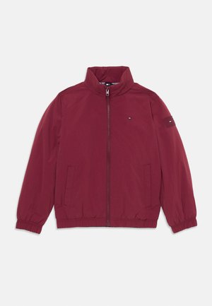 Chaqueta bomber burdeos con cremallera frontal, puños elásticos, dos bolsillos laterales y un parche con el logotipo en la manga. Tejido suave, diseño casual.