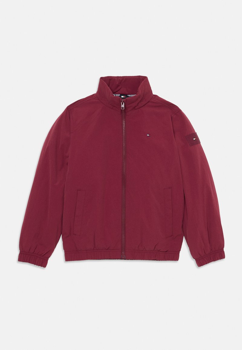 Giacca bomber bordeaux con zip frontale, polsi elasticizzati, due tasche laterali e una toppa con logo sulla manica. Tessuto morbido, design informale.