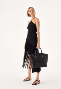 Musta ribbineulottu mekko, jossa on hapsureuna, yhdistetty tasapohjaisiin sandaaleihin ja suuriin mustiin kudottuihin olkalaukkuihin, joissa on kaksinkertaiset kahvat.