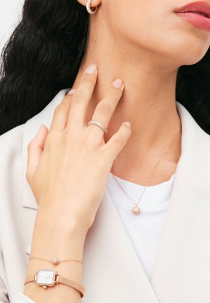 Rose gold watch with mesh band, sparkling ring, and pendant necklace with round stone, all displayed on a hand against a light background.