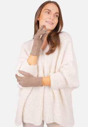 Braune Handschuhe aus weichem Material, mit glatter Oberfläche und tailliertem Design, kombiniert mit einem lockeren, strukturierten weißen Sweater.