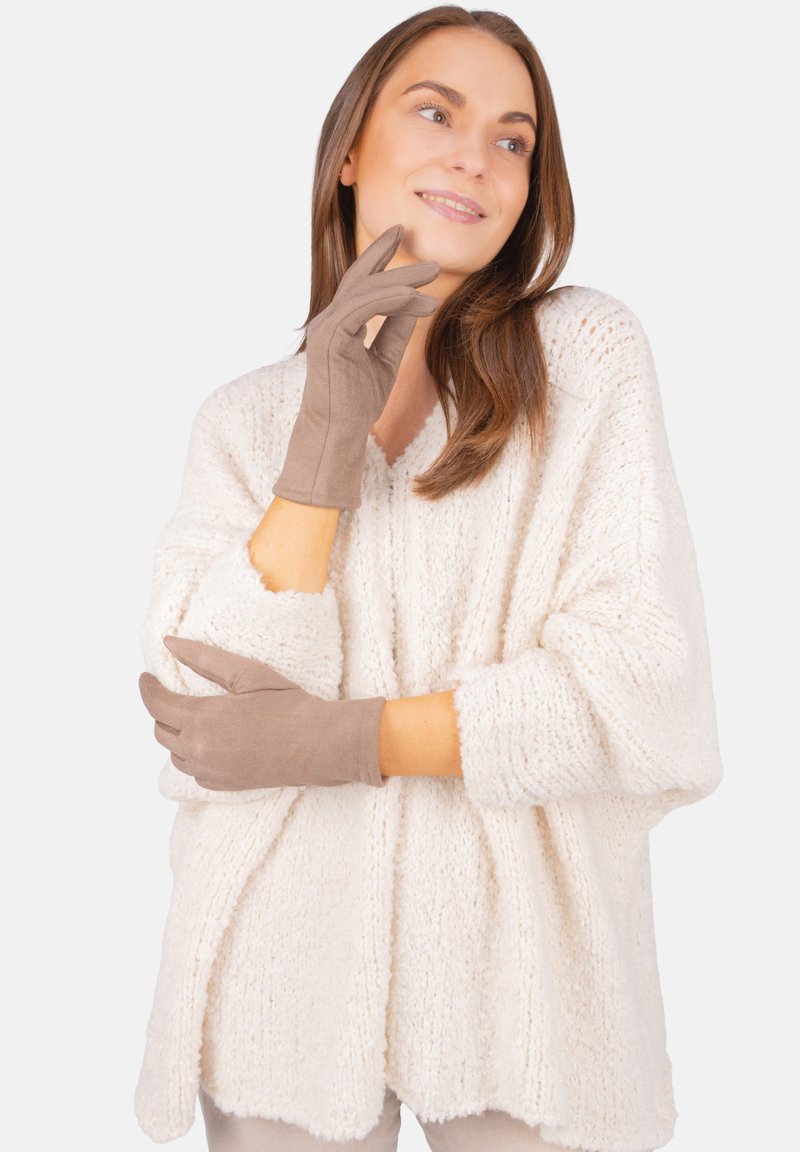 Braune Handschuhe aus weichem Material, mit glatter Oberfläche und tailliertem Design, kombiniert mit einem lockeren, strukturierten weißen Sweater.