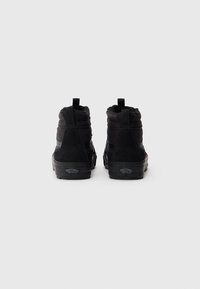 Pari di sneakers alte nere Vans viste da dietro su uno sfondo bianco semplice.