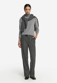 Grau-turtleneck Sweater mit langen Ärmeln, kombiniert mit hochgeschnallten grauen Hosen. Ein dunkelgraßer Schal hängt über den Schultern.