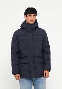 Navy blue puffer jacket with a high collar, zip and snap closure, front pockets, and elastic cuffs. Smooth texture, padded design for warmth.