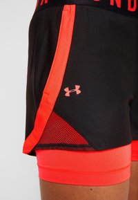 Herrarnas träningsshorts har en svart kropp med ljusa orange inslag, meshpaneler och en Under Armour-logotyp i rosa på sidan.