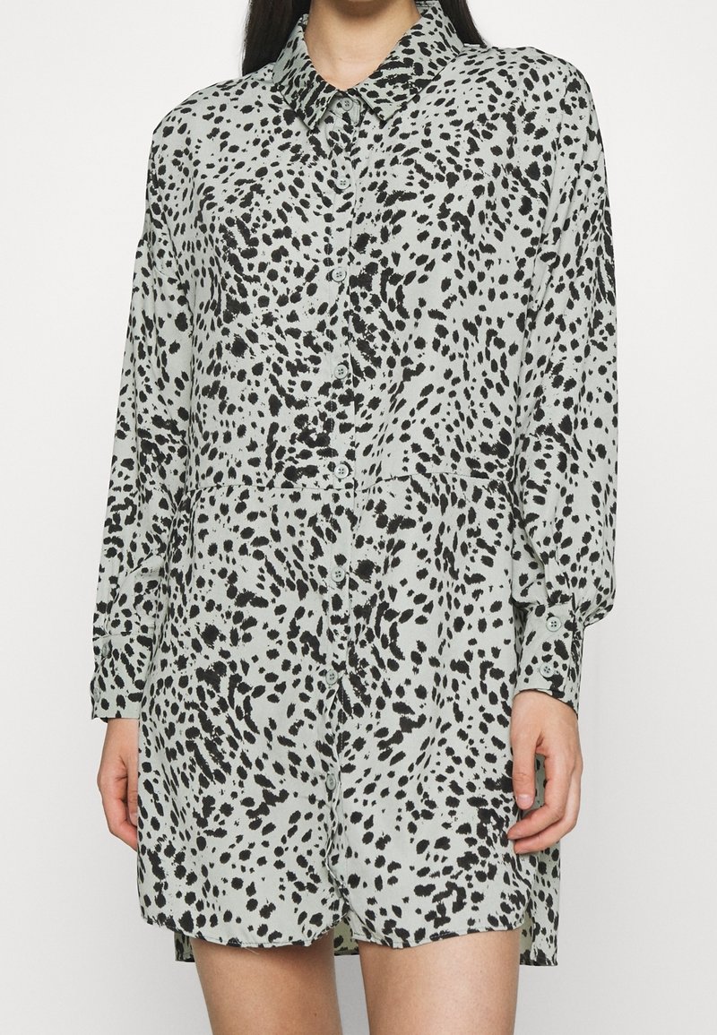 Robe à manches longues boutonnée avec un motif tacheté noir et blanc, portée par une personne avec les mains et les jambes visibles.