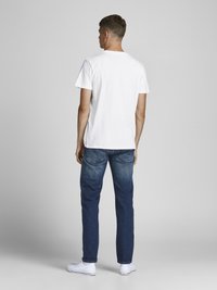 Camiseta blanca de manga corta, corte estándar, combinada con jeans de denim azul. Diseño sencillo, tejido suave, esquema de colores neutro, llevada con zapatillas blancas.