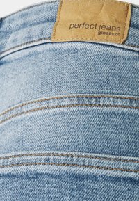 Vaaleansiniset farkut, joissa on nahkaleima, jossa lukee "perfect jeans" ja "ginatricot", näkyvät saumat ja kaksi takataskua.