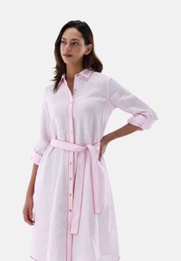 Abito in lino rosa chiaro con maniche lunghe, bottoni bianchi e una cintura rosa. Presenta piping rosa a contrasto lungo il colletto e le maniche.