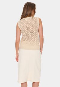 Top tricotaj bej fără mâneci, cu un model delicat de dantelă și tiv ribbed, asociat cu o fustă midi crem dintr-un material neted și elastic.